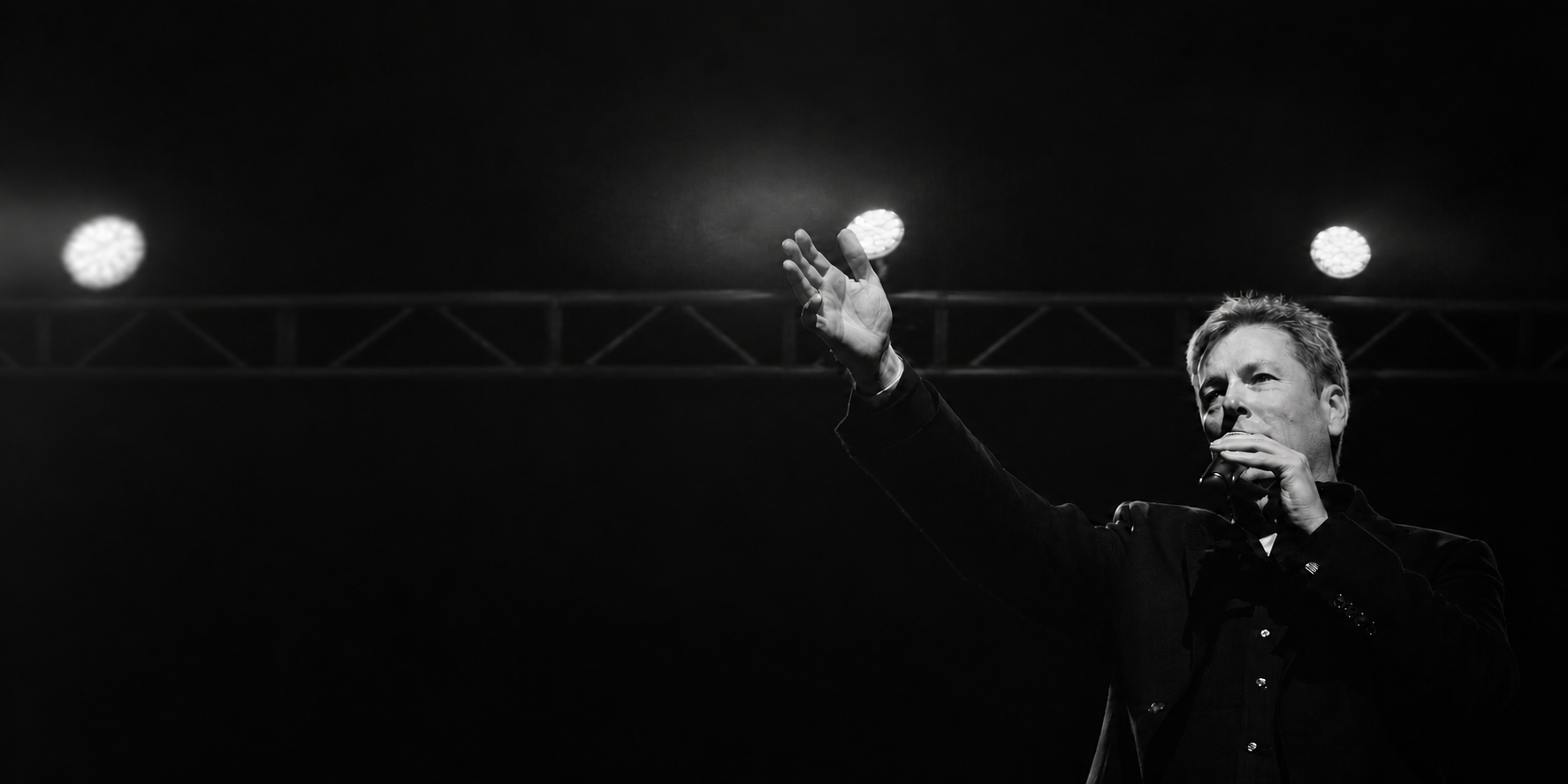 Russ Lorenson performing onstage with one hand raised, in black and white.